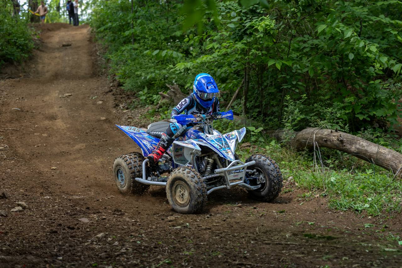 ATV rider cresting a sandy jump in the woods
